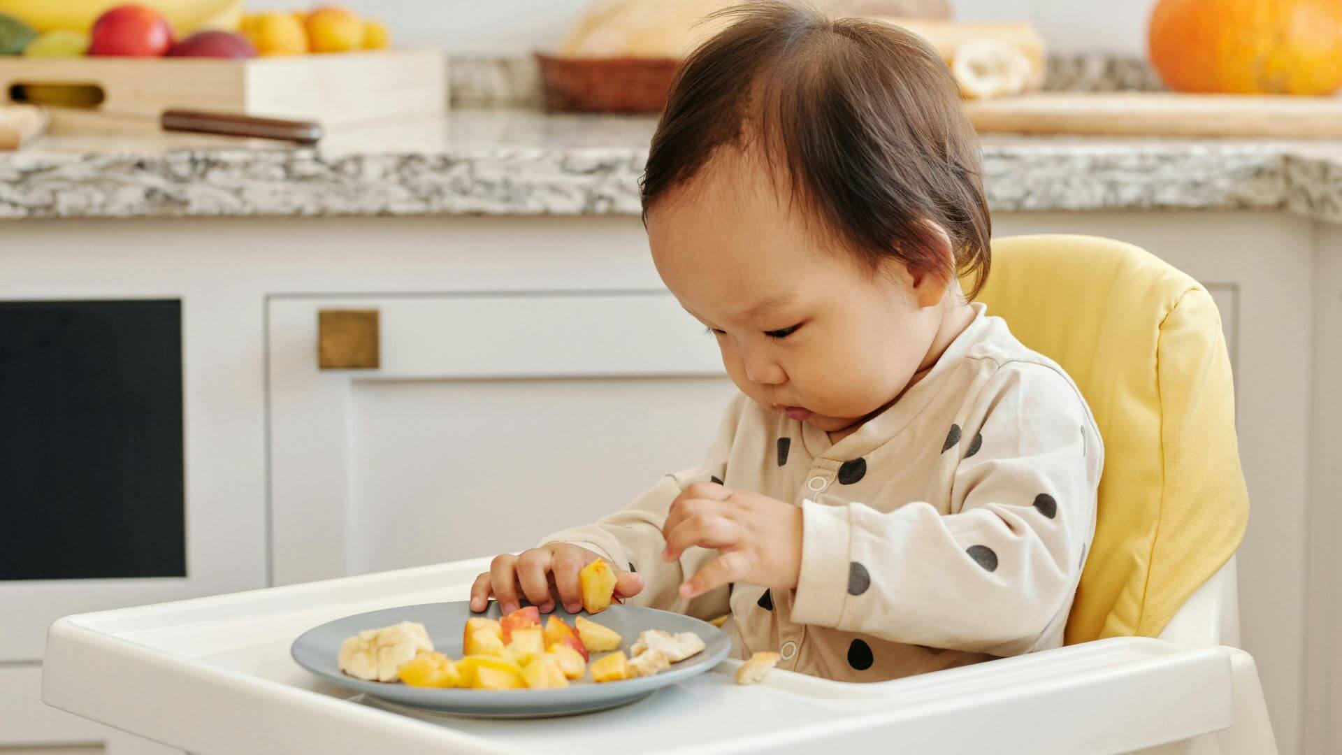 Baby on a highchair eating chopped fruit