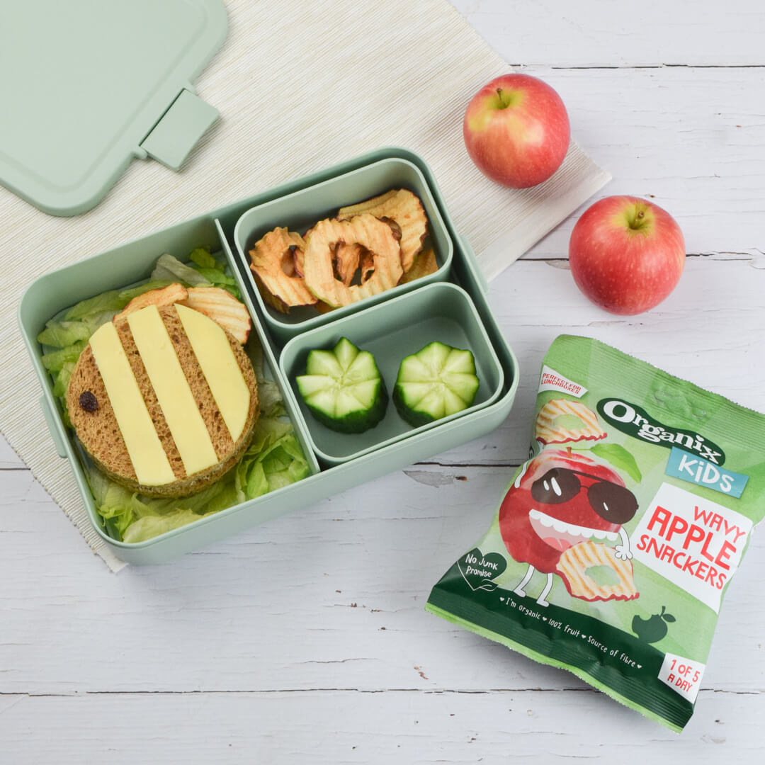 A bento style lunch box with a fun cream cheese sandwich cut to look like a bee, Organix wavy apple snackers and cucumbers in fun shape to look like flowers