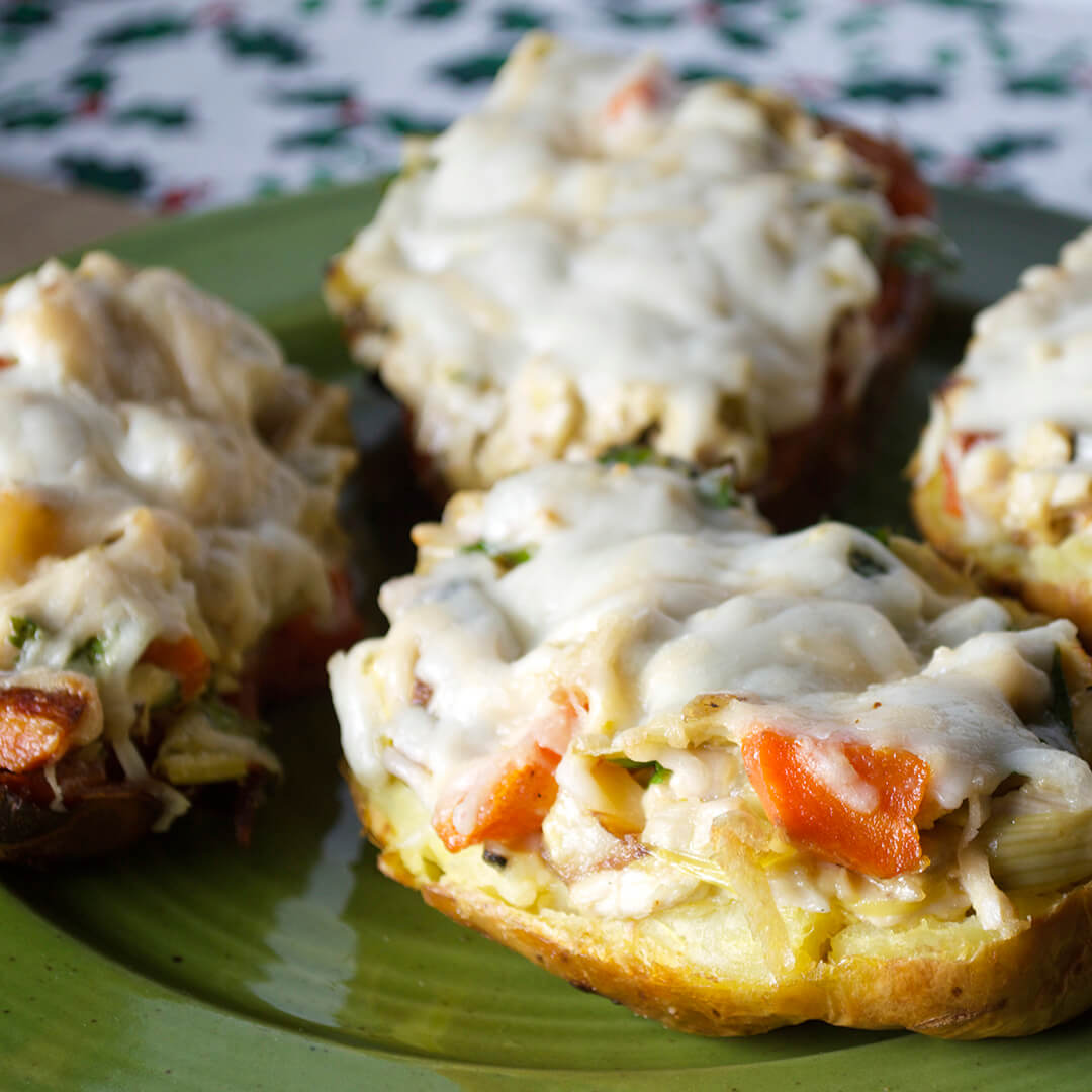 A halved jacket and sweet potato filled with vegetables and meat in a creamy sauce and topped with cheese