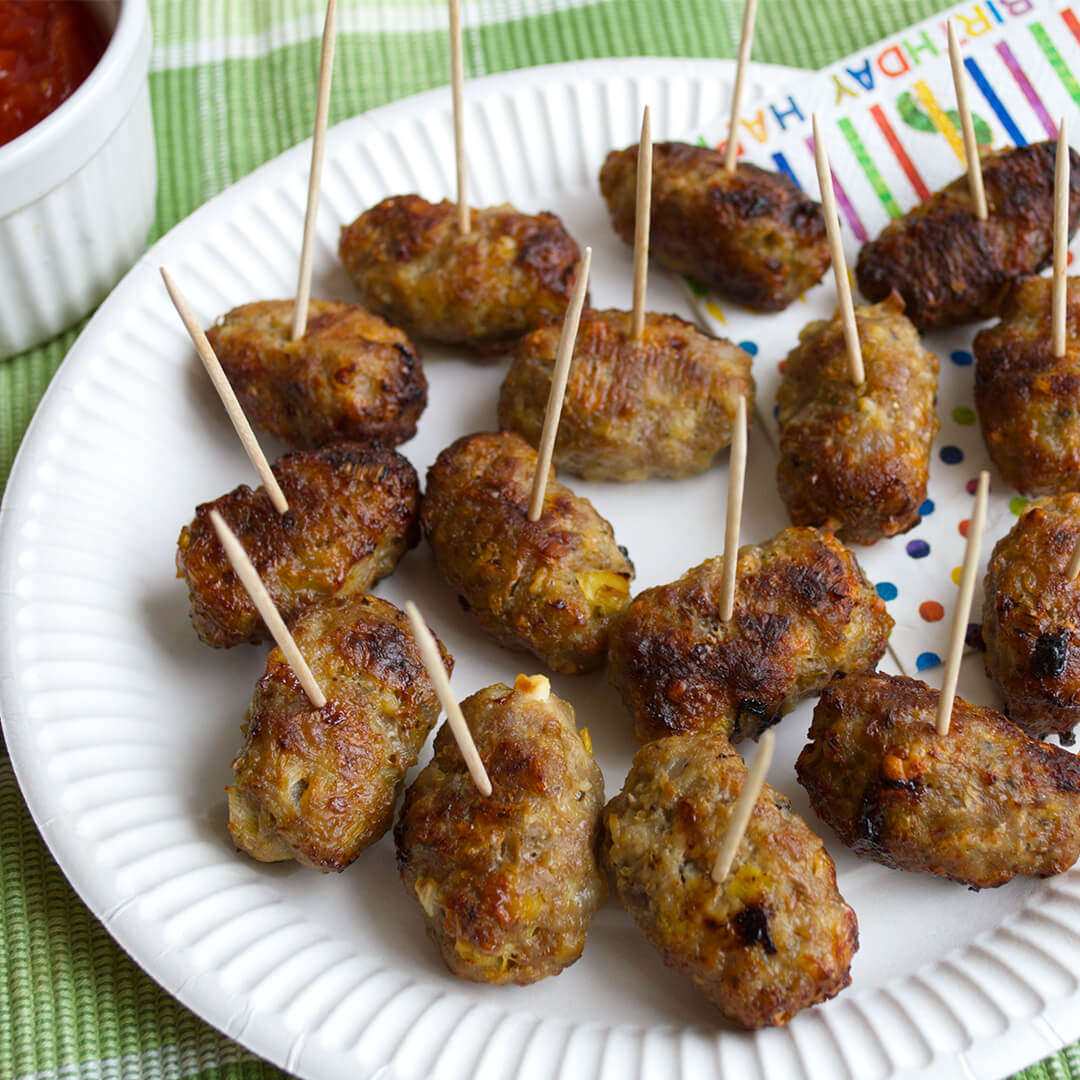 Pork, Leek & Feta Cocktail Sausages on a plate next to a tomato dip