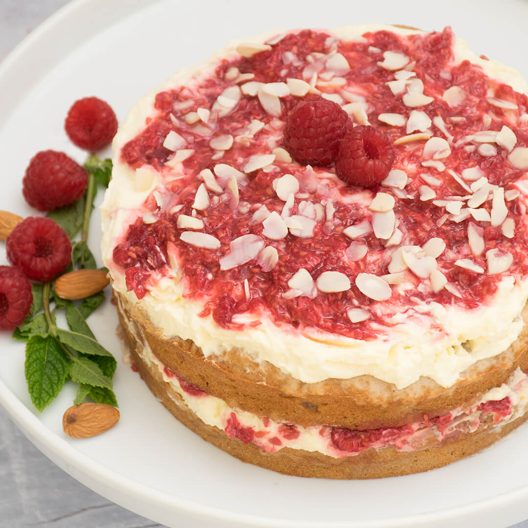Raspberry Victoria Sponge Cake on a cake stand with some raspberries