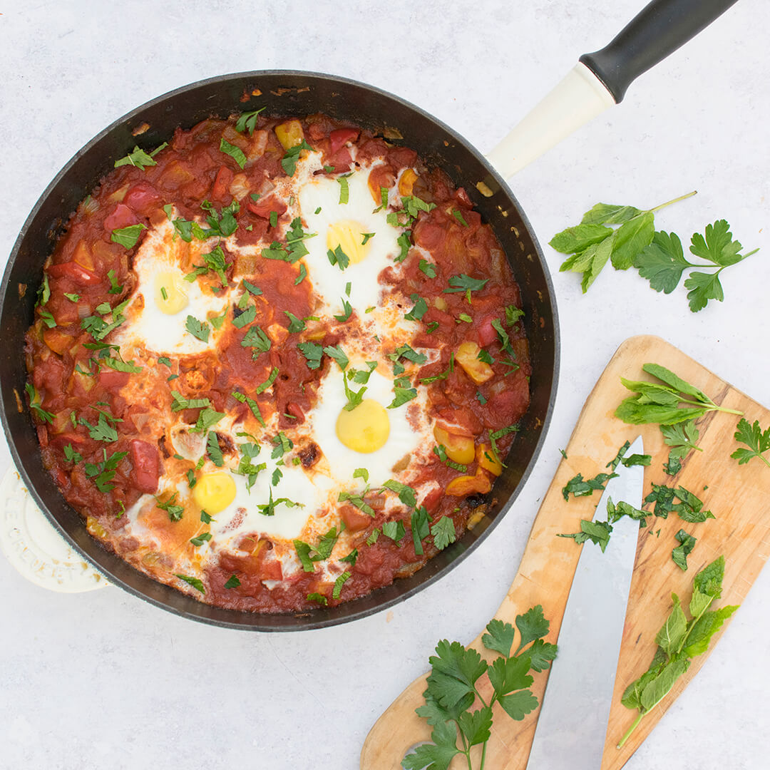 Shakshuka in a pan with a chopping board with chopped parsley next to it