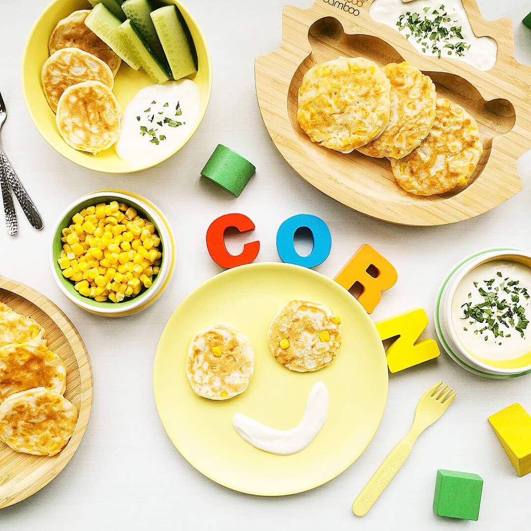 4 servings of sweetcorn fritters served with a yoghurt dip and next to a bowl of sweetcorn