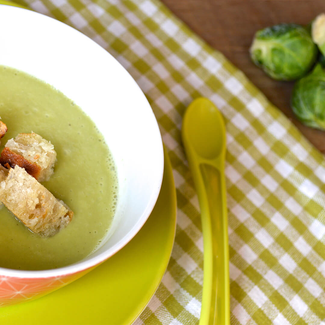 A bowl of Sprout Soup With Cheesy Croutons next to some Brussels sprouts