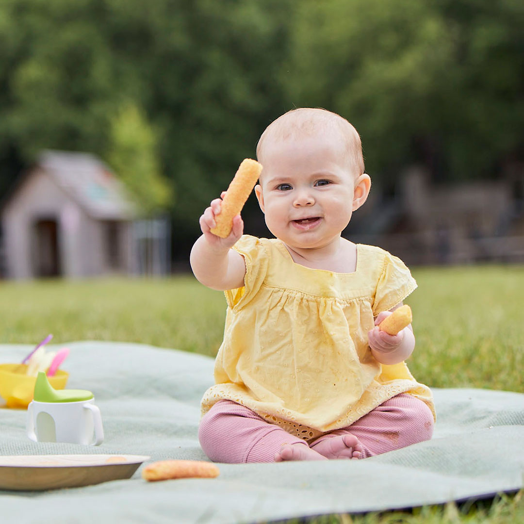 Baby eating snacks, on a picnic blanket
