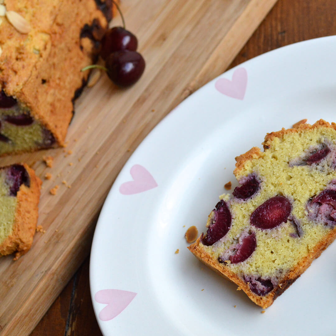 A slice of cherry almond next to a Cherry Almond Loaf and some fresh cherries