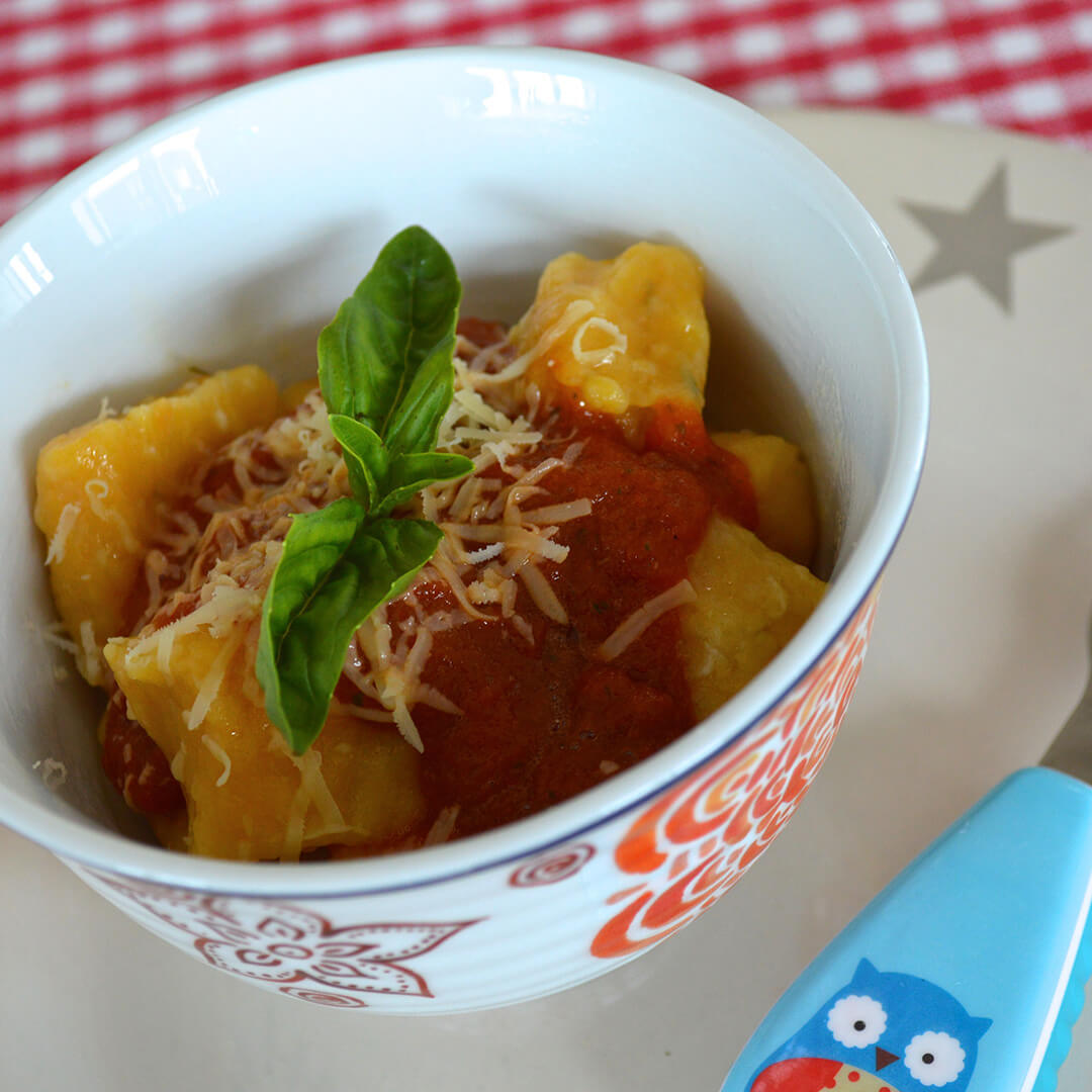 A bowl of Gnocchi With Tomato & Basil topped with cheese and fresh basil leaves