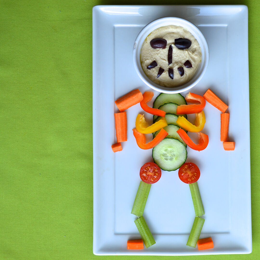 Spooky Skeleton Platter with a vegetable body and a bowl of hummus topped with olives to make a face