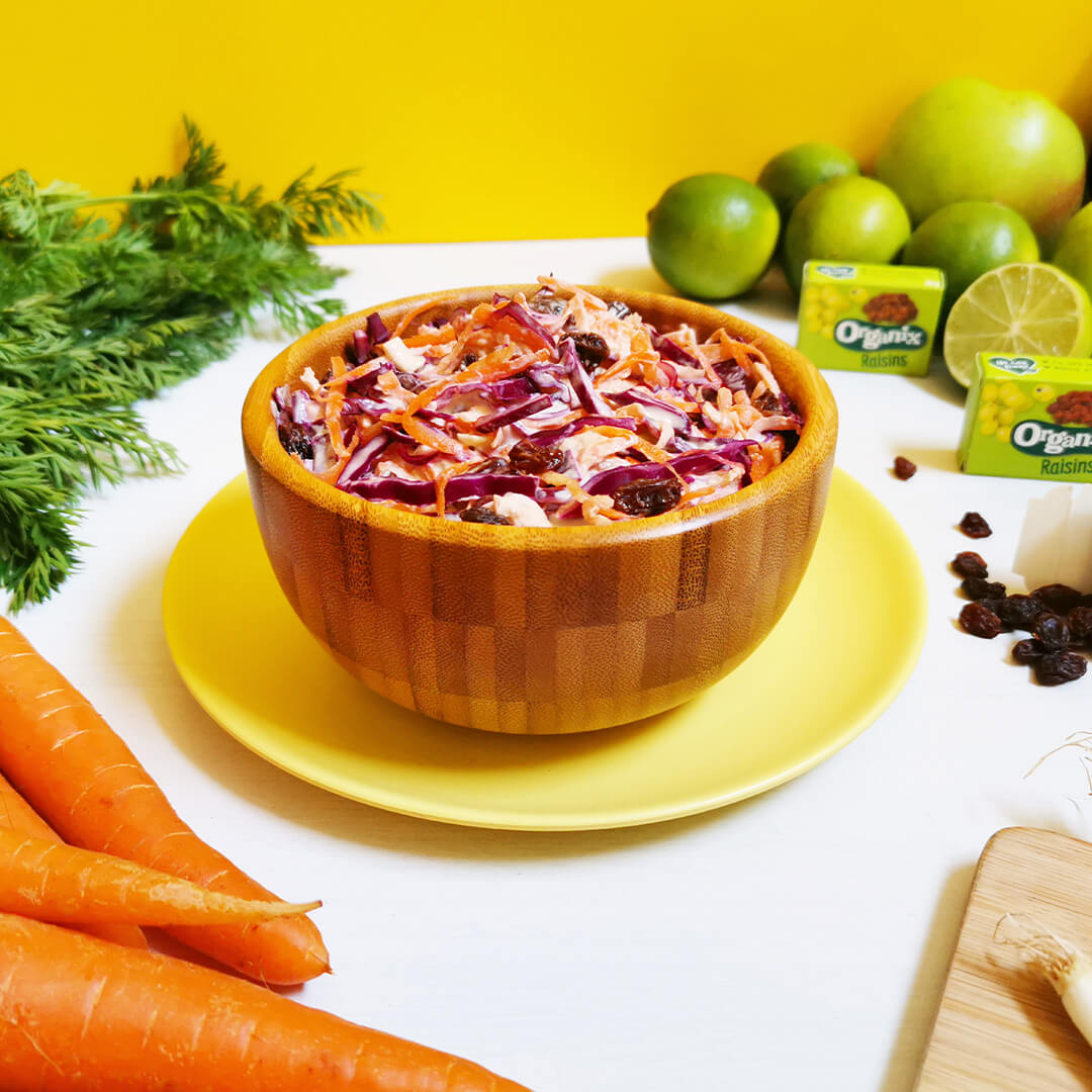 A bowl of apple and red cabbage coleslaw next to some limes and carrots