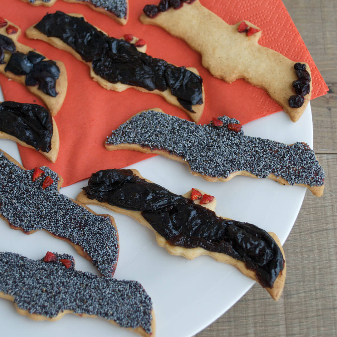 A plate of bat shaped biscuits decorated with dried berries and seeds