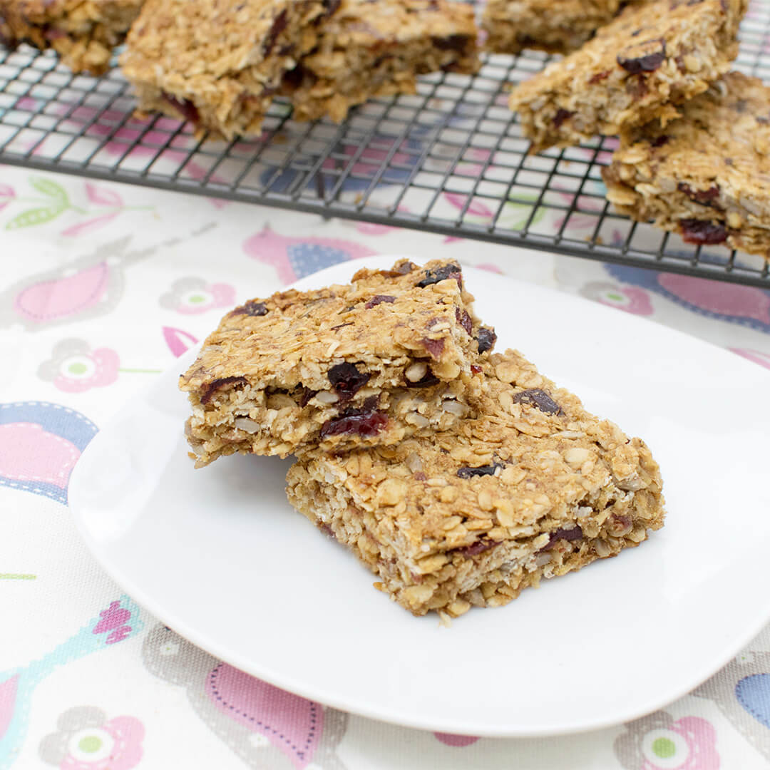 A plate with 2 cranberry seed bars, next to a cooling rack of cranberry seed bars