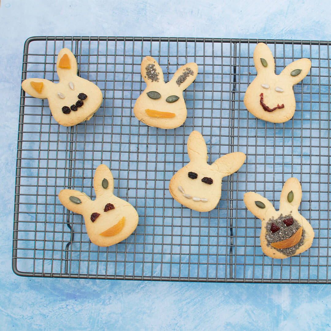 A cooling rack with 6 bunny shaped biscuits decorated with dried fruit and seeds