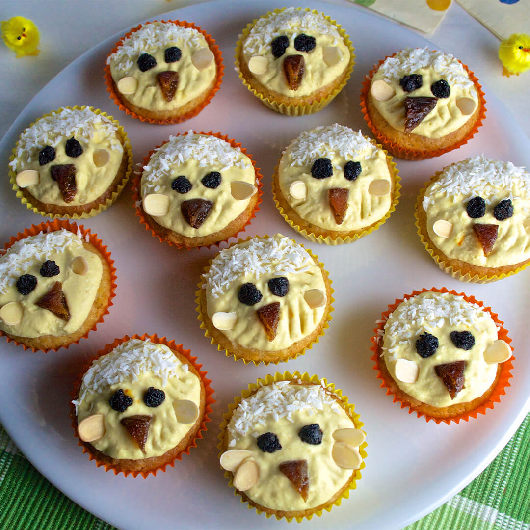 A plate of 12 cupcakes decorated with fruit and desiccated coconut to look like chicks