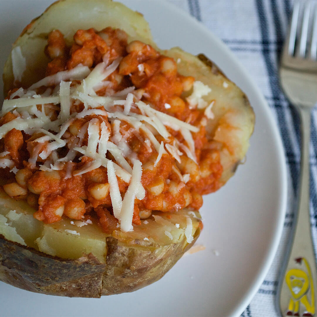 A plate with a jacket potato topped with homemade baked beans and grated cheese