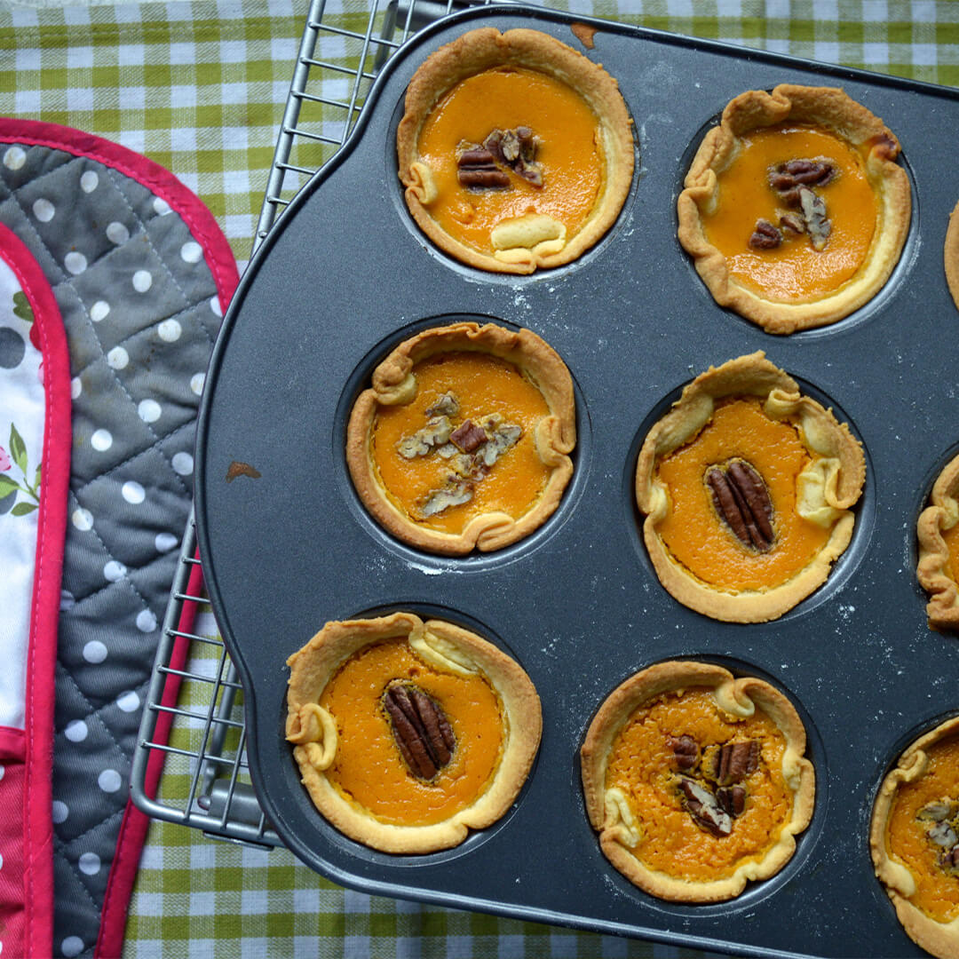A cupcake tin of Mini Maple & Pumpkin Pies topped with pecans
