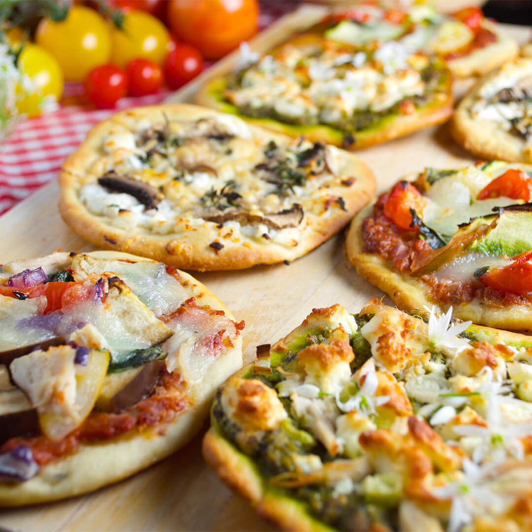 A chopping board with 8 mini pizzas topped with various toppings