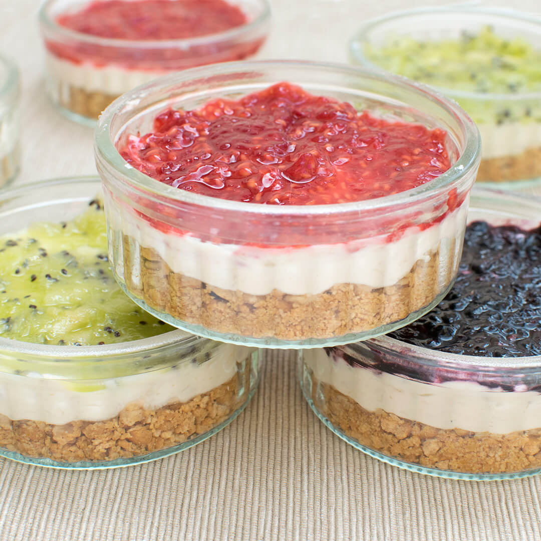 5 Organix cheesecakes in small ramekins, 2 topped with kiwi puree, 2 topped with strawberry and raspberry puree and 1 with blackberry puree