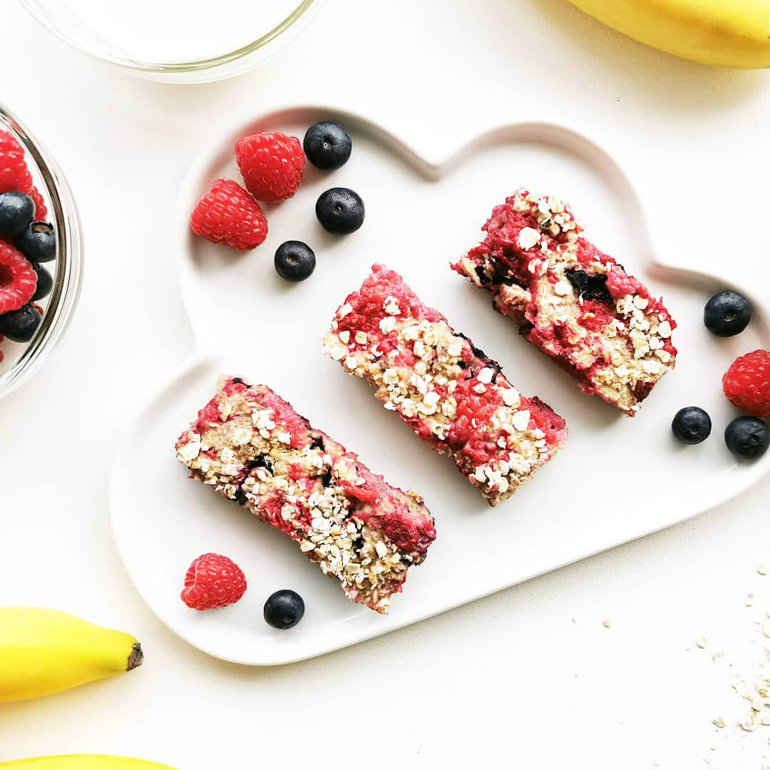 A plate of porridge fingers served with raspberries and blueberries, next to some bananas