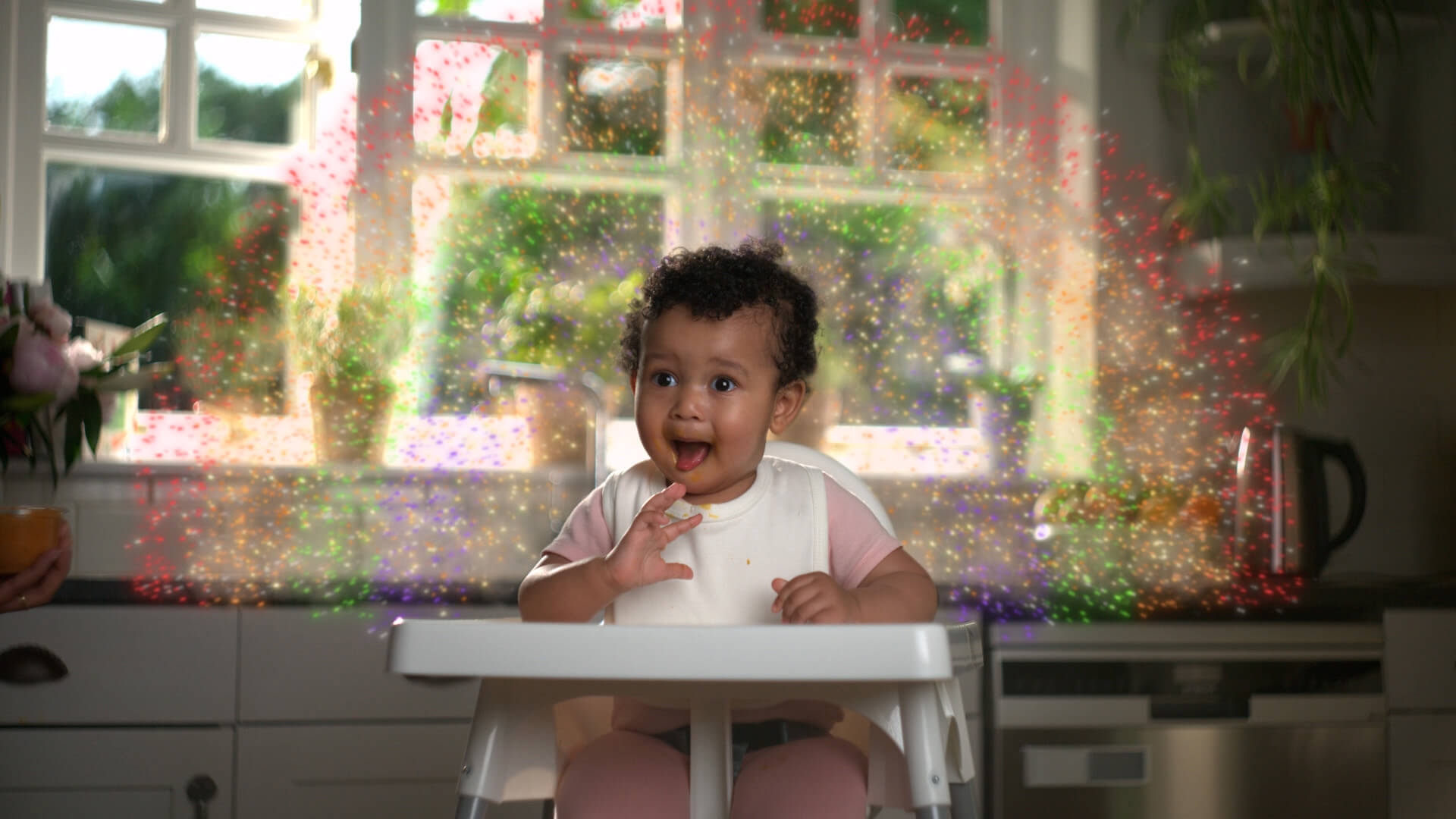 A baby sitting on a high chair with an animated rainbow around her in red, orange, green and blue