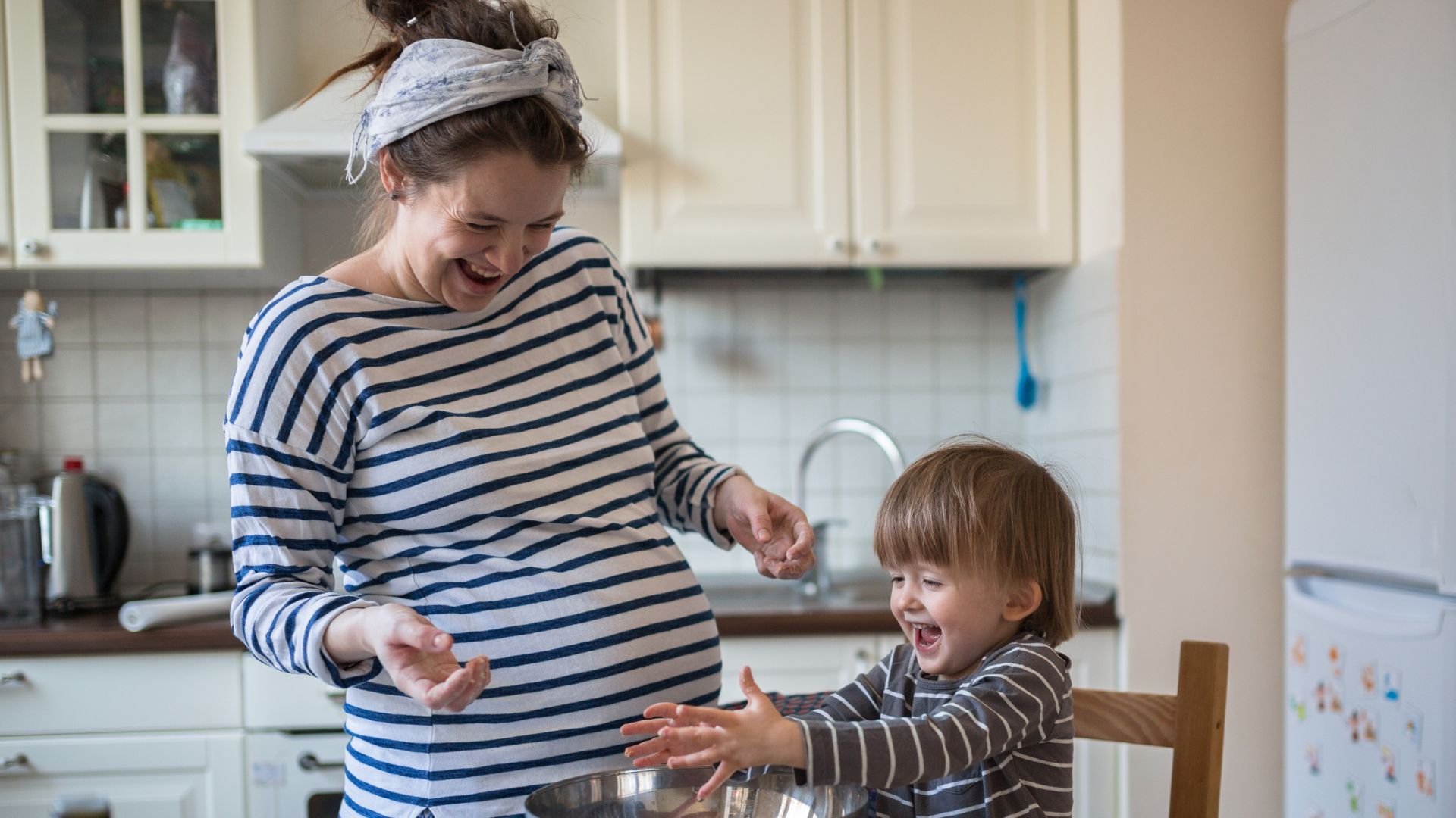 Young pregnant mum in stripy top baking in the kitchen with her toddler child also wearing a stripy top
