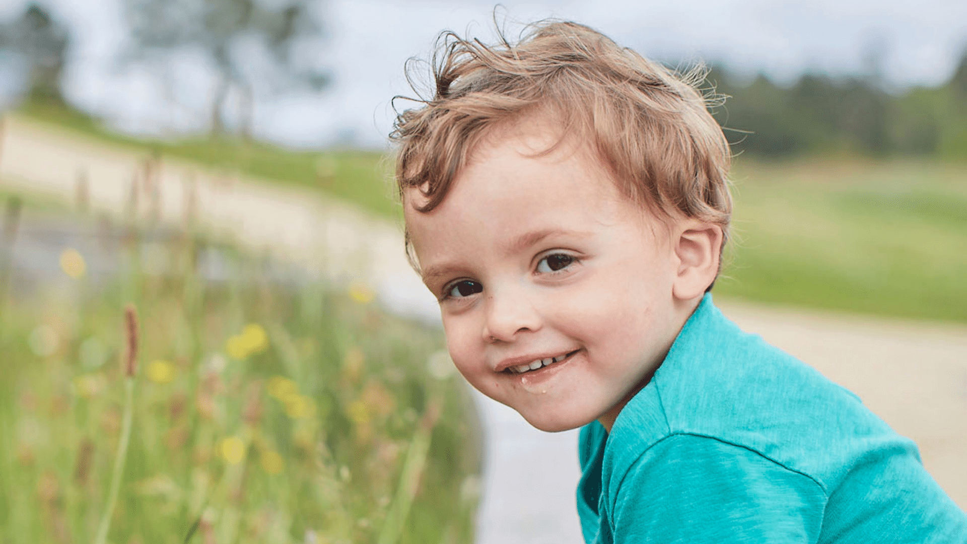 Toddler at the park wearing a green t-shirt looking at the camera and smiling