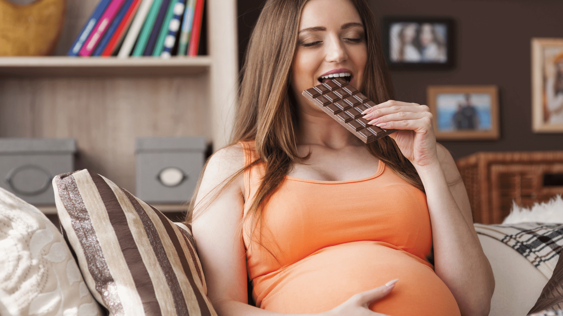 Pregnant woman sitting on sofa eating chocolate