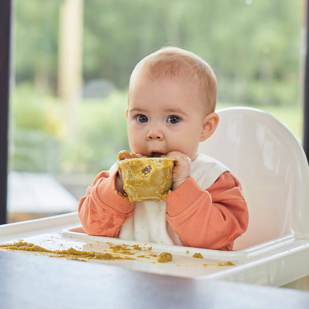 A baby eating from a tub of food