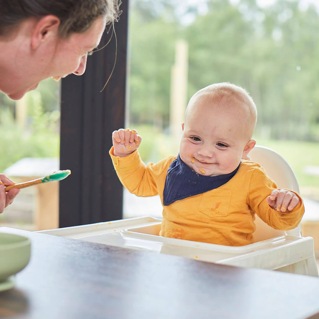 A smiling baby sitting in a high chair and being fed