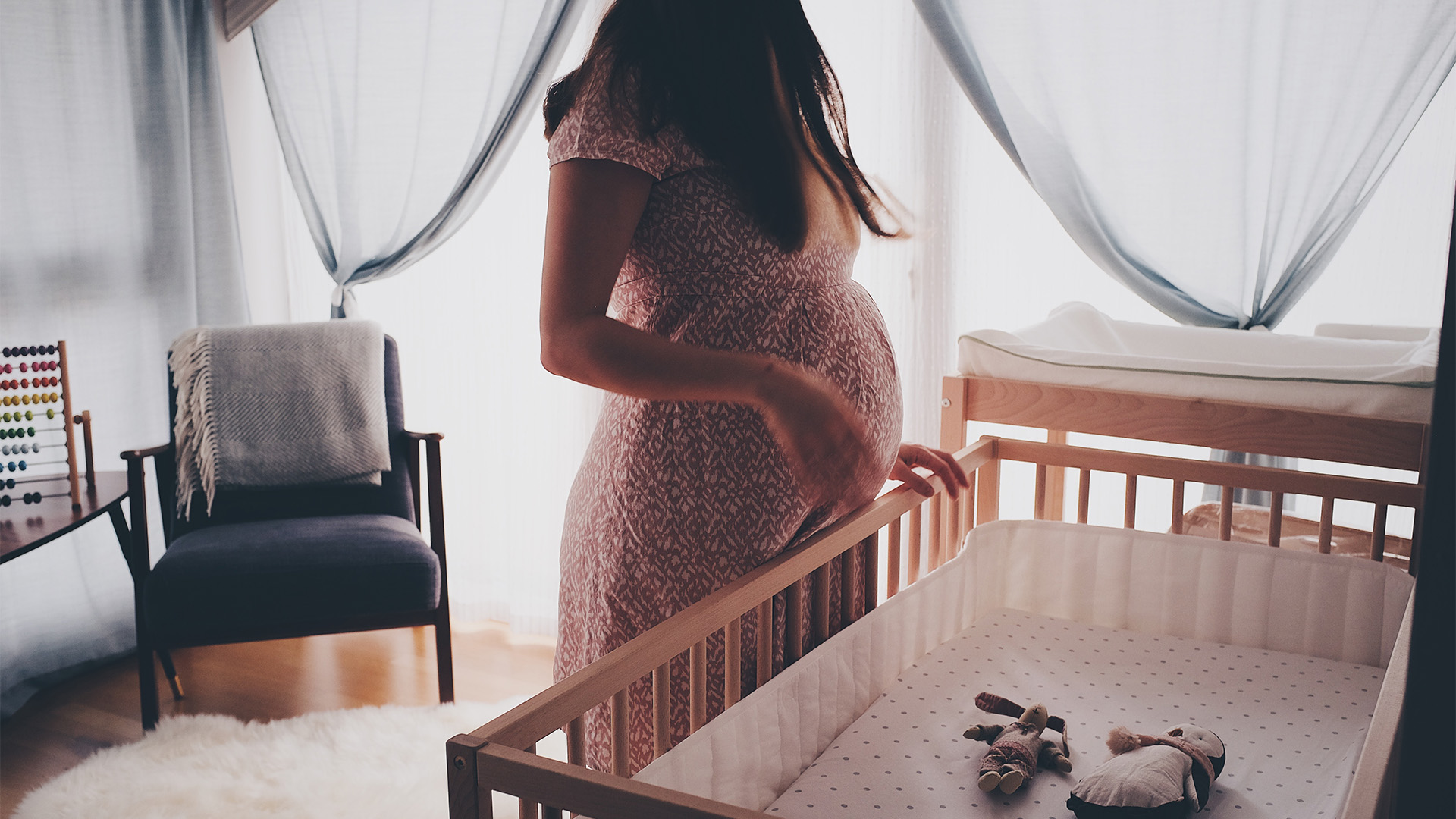 A pregnant woman in a nursery, standing over a crib/cot