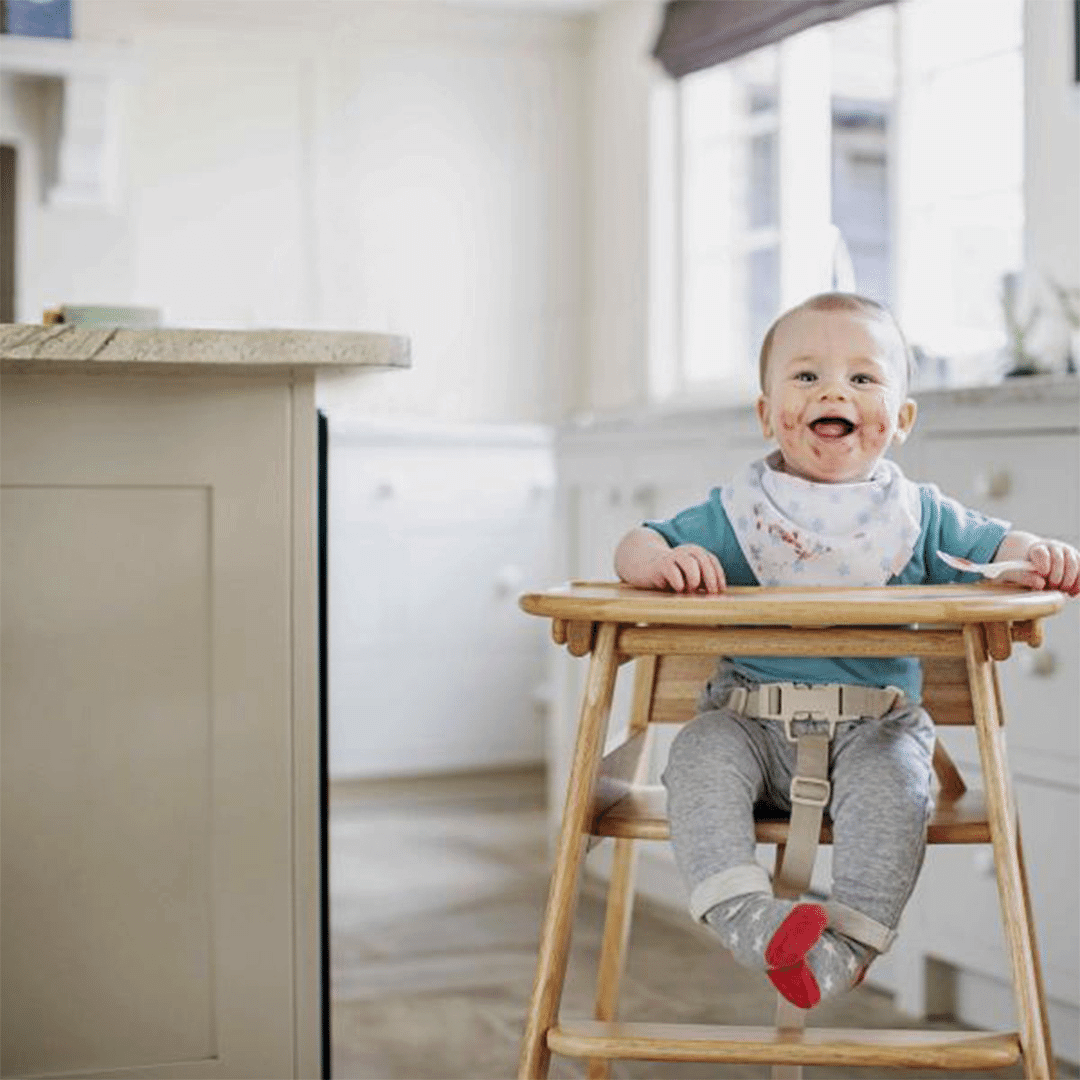 A smiling baby on a wooden highchair