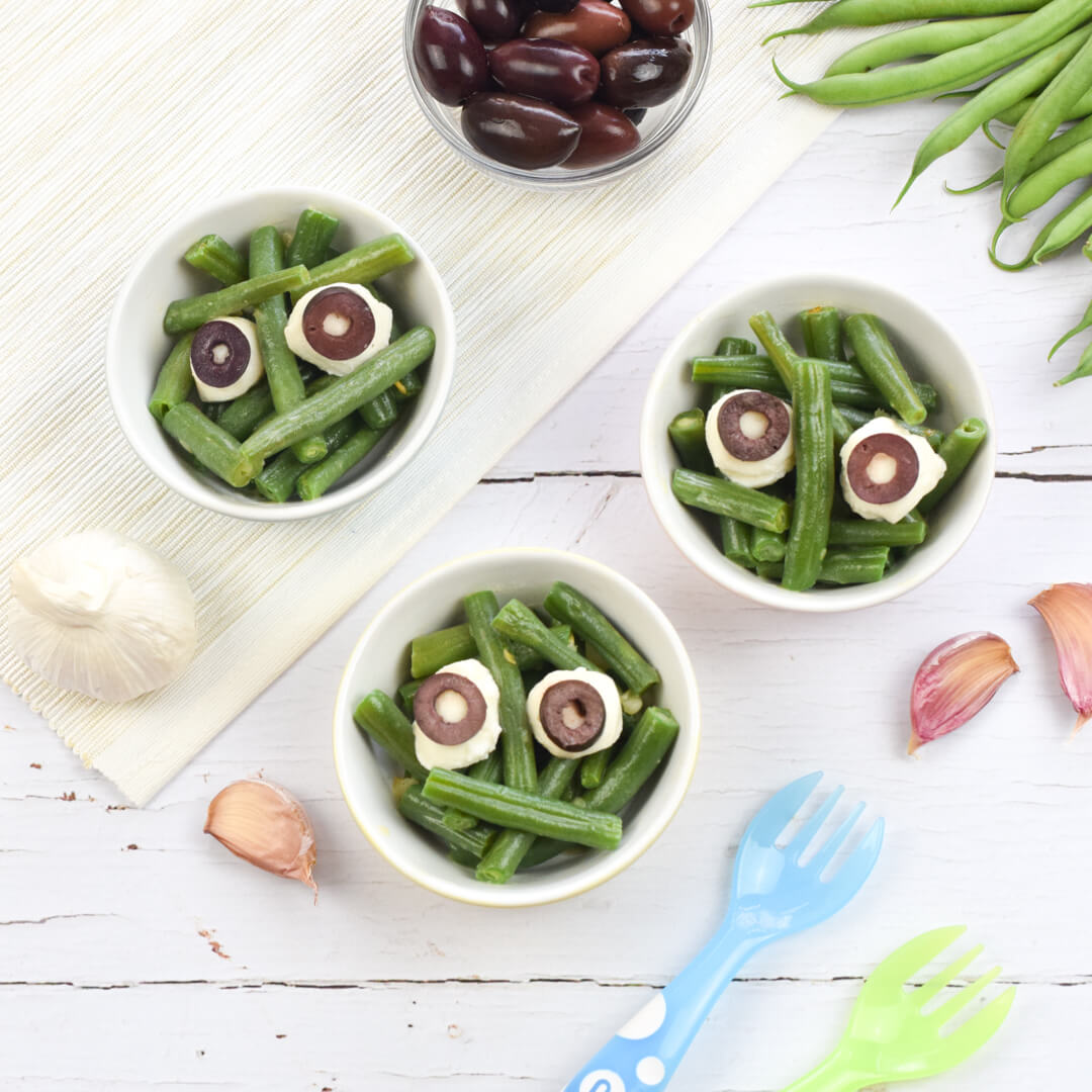 3 small bowls of green bean monsters: green beans topped with small mozzarella bowls and sliced black olives to create eyes