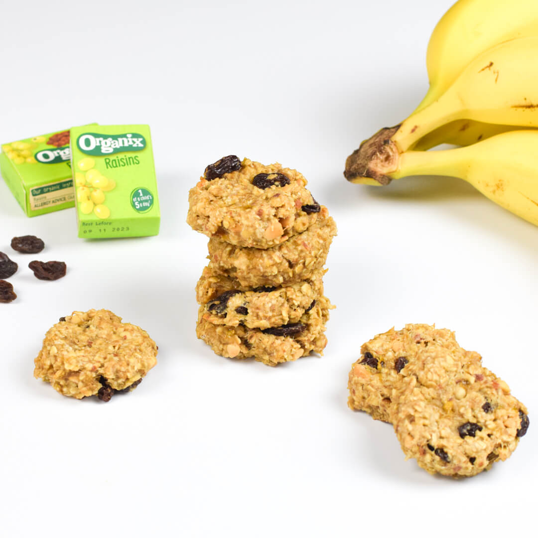 A stack of peanut butter raisin cookies next to some Organix raisins and a bunch of bananas
