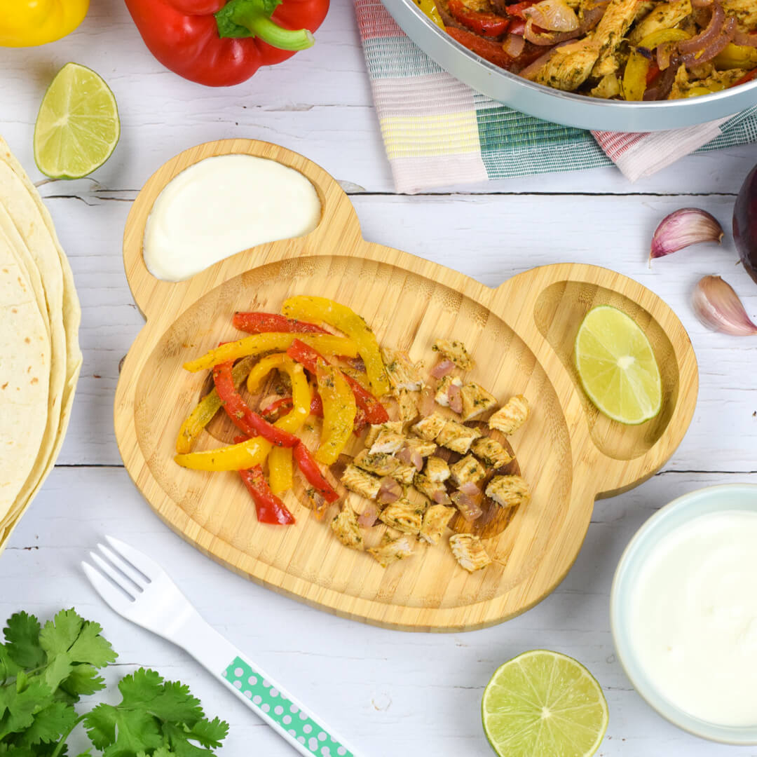 A serving of chicken and pepper fajitas with sour cream and a lime wedge
