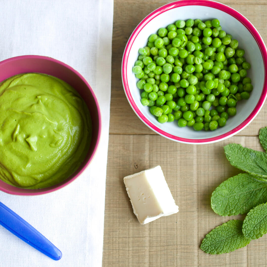 A bowl of Pea & Mint Puree with Goat Cheese next to a bowl of peas, some goats cheese and mint leaves