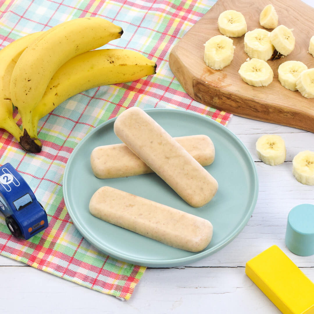 A serving of peanut butter yoghurt bites next to a bunch of bananas and a chopping board with banana slices