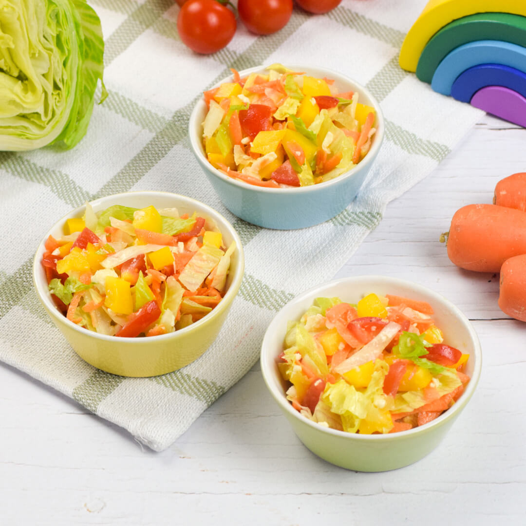 3 small bowls of rainbow salad (lettuce, pepper, carrot, tomato and mozzarella) next to some carrots, lettuce and cherry tomatoes