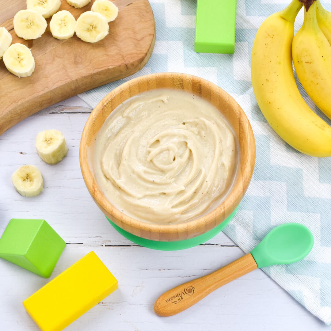 A bowl of vanilla nice cream next to a bunch of bananas and a wooden chopping board with sliced banana