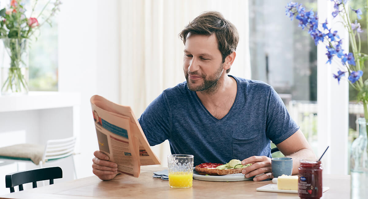 a man at a table reading a newspaper while eating breakfast