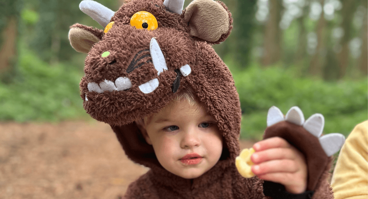 Child dressed in a Gruffalo costume and holding an Organix Gruffalo Claw snack in their hand and showing to the camera