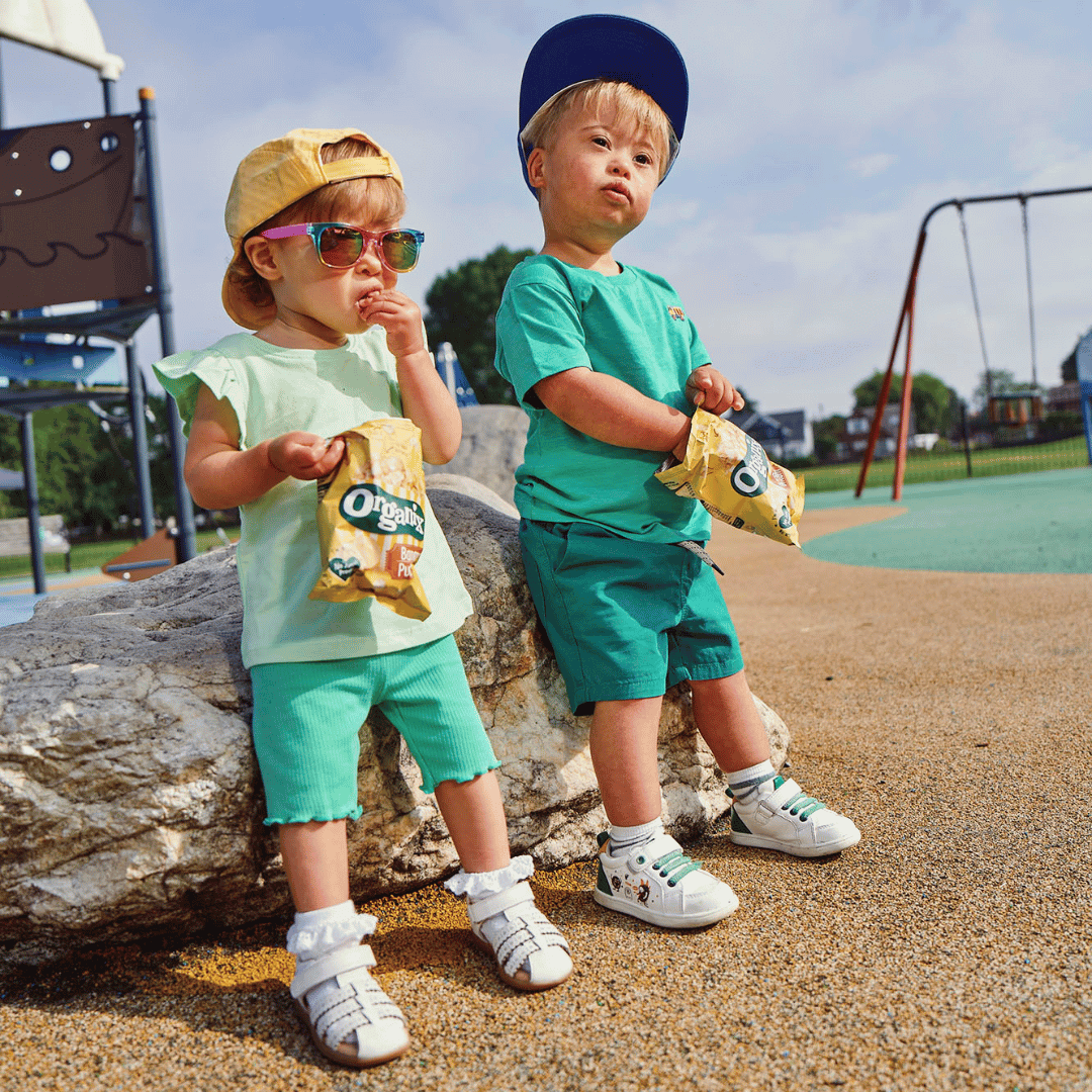 Two cool kids at the park wearing sun hats and sun glasses and eating Organix snacks