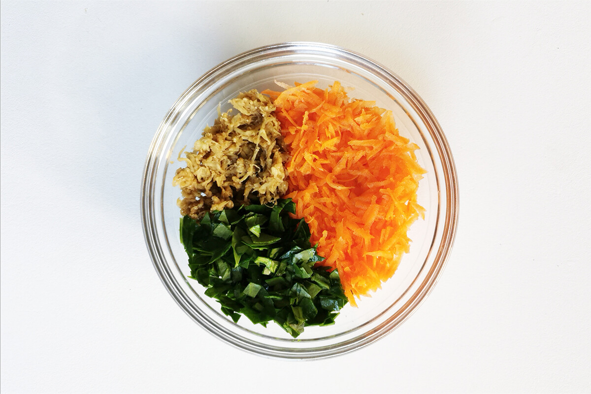 A glass bowl with grated carrot, grated aubergine and chopped spinach