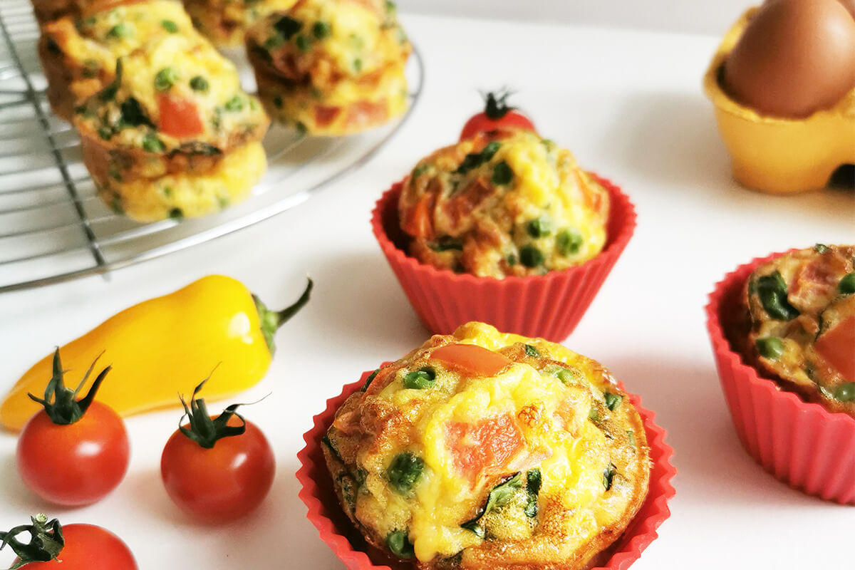 Aubergine muffins next to some cherry tomatoes and a case of eggs
