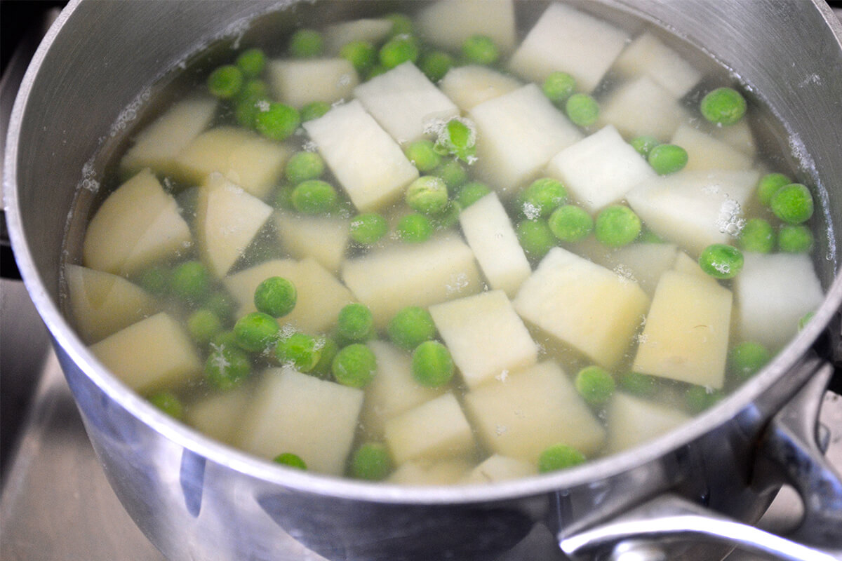 A saucepan with water potatoes and peas