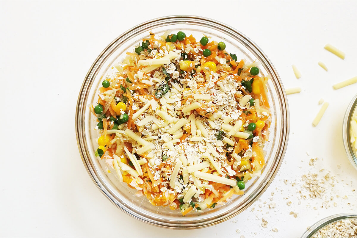 A glass bowl with mashed sweet potato, salmon, vegetables, oats and grated cheese