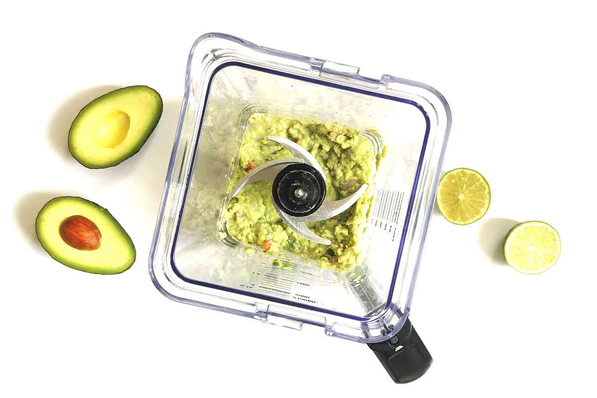 Guacamole in a blender, next to a halved avocado and halved lime