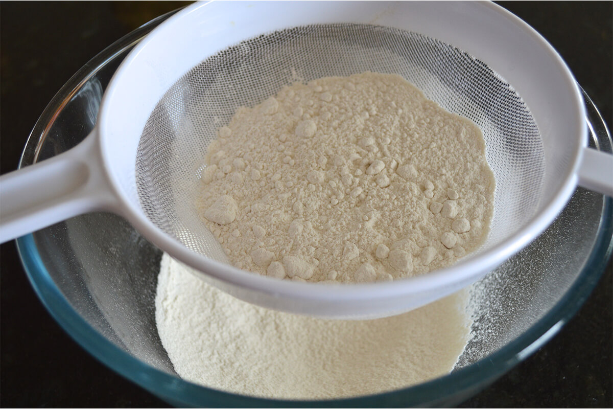 Flour being sieved over a glass bowl