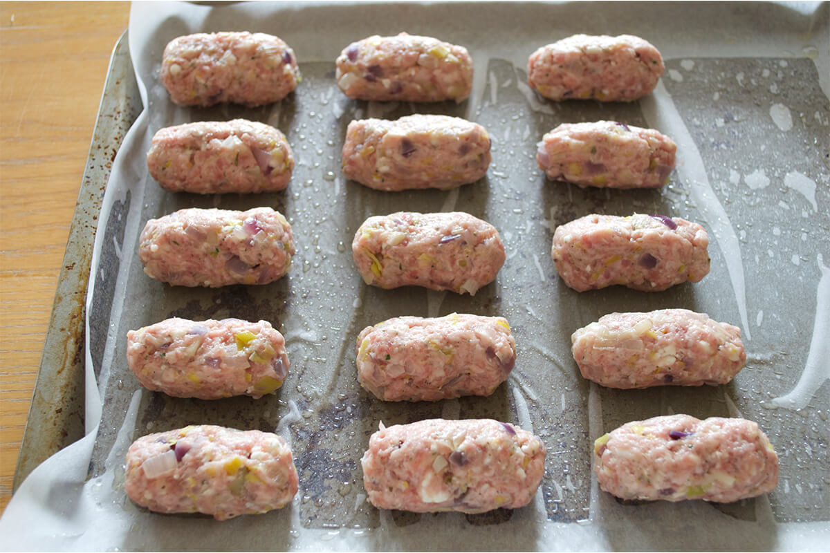 Uncooked Pork, Leek & Feta Cocktail Sausages on a lined baking tray