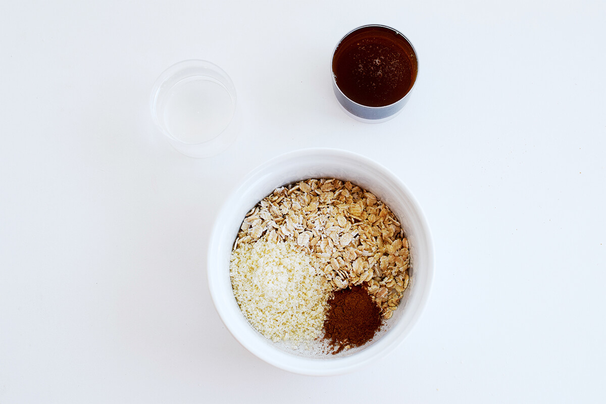 A bowl of crumble mix - oats, ground almonds and cinnamon powder next to some melted butter combined with maple syrup