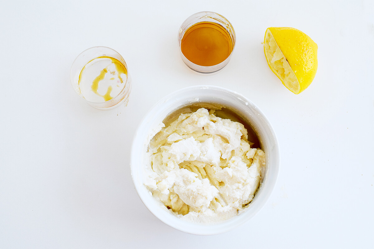 A bowl of mascarpone next to an empty container, a container of maple syrup and a squeezed lemon