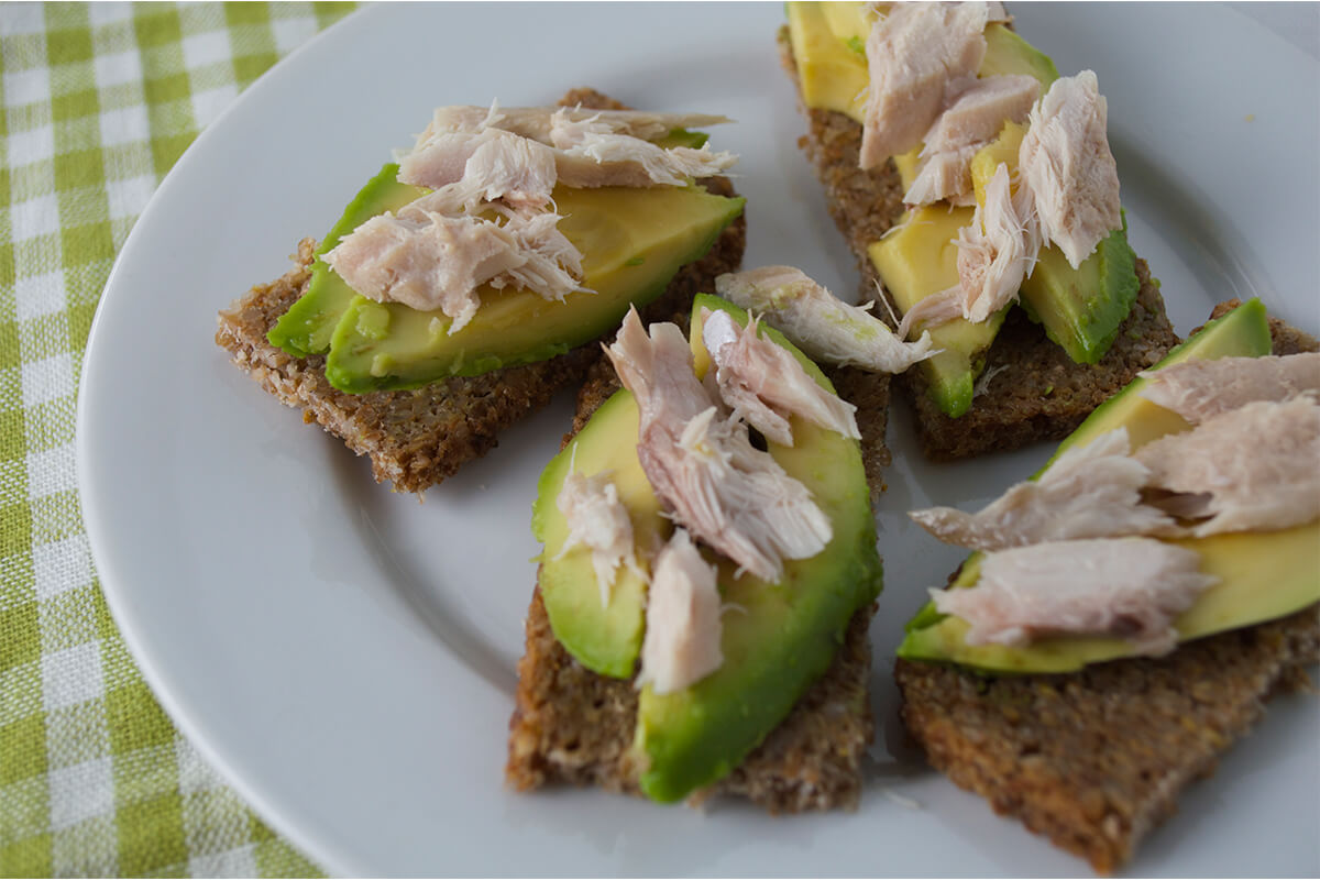 A slice of rye bread cut into quarters and topped with avocado and mackerel 
